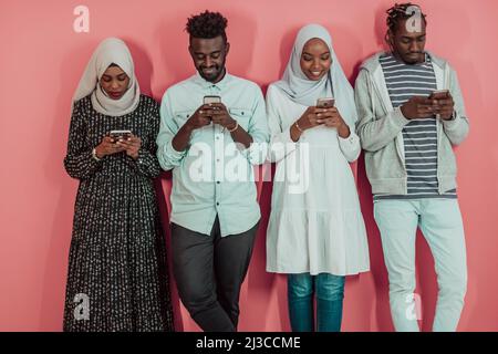 Eine Gruppe afrikanischer muslimischer Studenten benutzt Smartphones, während sie vor einem rosa Hintergrund stehen Stockfoto