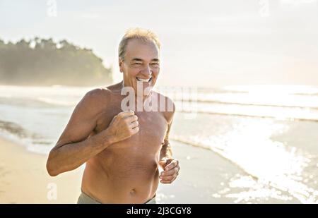 Ältere Männer, die sich am Strand bei Sonnenuntergang beim Joggen Vergnügen Stockfoto