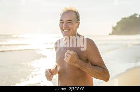 Ältere Männer, die sich am Strand bei Sonnenuntergang beim Joggen Vergnügen Stockfoto