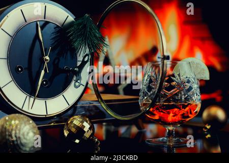 Eine Tischuhr mit einer offenen Glasabdeckung, umgeben von Weihnachtsdekorationen vor dem Hintergrund eines Feuers. Stockfoto