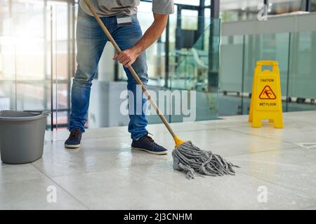 Lassen Sie den Boden makellos. Aufnahme eines nicht erkennbaren Mannes, der die Büroetage wischt. Stockfoto