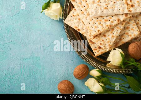 Konzept der Passahfeier. Matzah, rote koschere Walnuss und Frühling schöne Rosenblüten. Traditionelles rituelles jüdisches Brot auf helltürkis oder blau Stockfoto