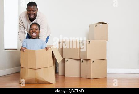Bereit, fertig, los. Aufnahme eines glücklichen jungen Vaters, der sich mit seiner Tochter anschob und sie in eine Kiste in ihrem neuen Zuhause schob. Stockfoto