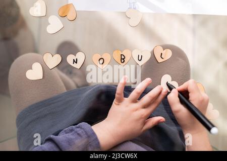 Blick von oben auf das anonyme Kind, das auf kleine Herzen schrieb, während es am Glastisch im Zimmer saß Stockfoto