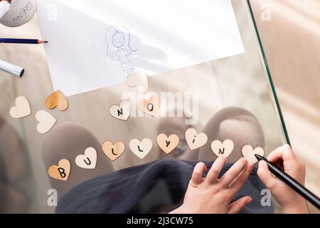 Draufsicht auf Crop anonymous Kid Writing No Mobbing Inschrift auf kleinen Herzen, während sie am Glastisch im Zimmer sitzen Stockfoto