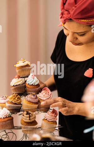Hispanische Frau im Kopftuch, die tagsüber in der Bäckerei Desserts auf den Tisch arrangierte Stockfoto
