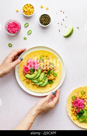 Hand of Crop anonyme weibliche berühren leckeren Taco mit reifen Avocado Scheiben und Kichererbsen Füllung serviert auf dem Tisch Stockfoto