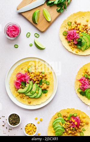 Draufsicht auf Tortillas mit in Scheiben geschnittenen Avocados und Kichererbsen auf weißem Hintergrund mit Limettenscheiben und grünem Pfeffer in der Küche Stockfoto