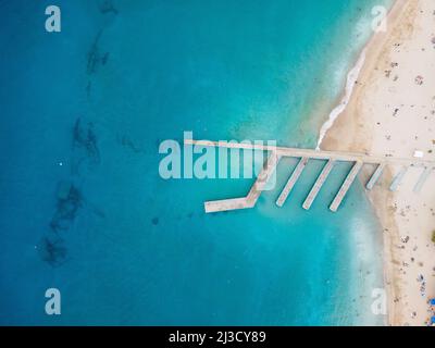 Luftaufnahme des Kais mit Wellenbrechern an der sandigen Küste, die vom türkisfarbenen Meerwasser in einem tropischen Resort gewaschen wird Stockfoto