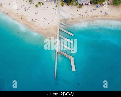 Luftaufnahme des Kais mit Wellenbrechern an der sandigen Küste, die vom türkisfarbenen Meerwasser in einem tropischen Resort gewaschen wird Stockfoto