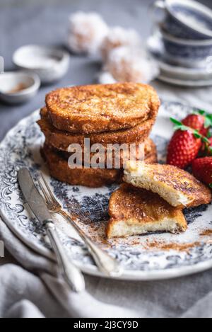 Leckeres französisches Toast mit reifen Erdbeeren, serviert auf Porzellanteller mit Besteck zum Frühstück am Morgen Stockfoto