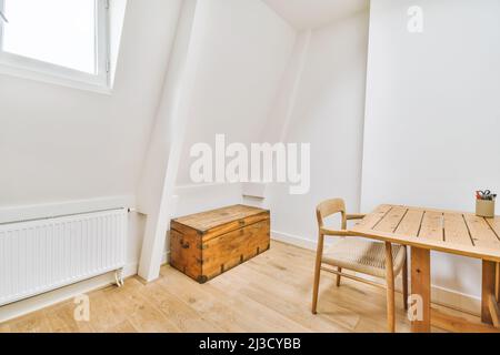 Altmodische Holzkiste in der Nähe von Stuhl und Tisch mit Schreibwaren in einem hellen Raum mit weißen Wänden und Fenster in der Wohnung Stockfoto