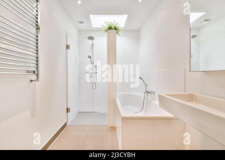 Weißes Keramikwaschbecken an der Wand mit Spiegel in der Nähe der Badewanne im hellen, geräumigen Badezimmer mit Duschkabine und gefliesten Wänden Stockfoto