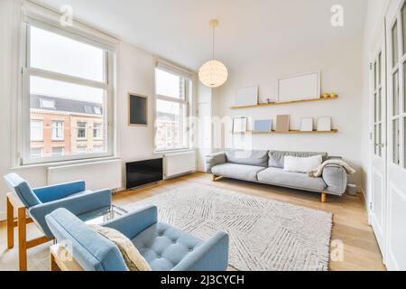 Komfortable Sessel und Sofa in der Nähe von Teppich in hellen geräumigen Wohnzimmer mit dekorativen Rahmen und modernen TV in der Wohnung platziert Stockfoto