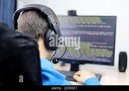 Programmierung, Cyberkriminalität und Hacking. Nicht erkennbarer Typ in Kopfhörern, der am Desktop-PC sitzt und den Standort- oder Anwendungscode auf dem Monitor hat Stockfoto