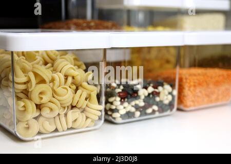 Transparente Behälter, gefüllt mit Nudeln, Hülsenfrüchten und Getreide, auf dem Regal in der Küche. Organisation der Lagerung von Massengütern Stockfoto