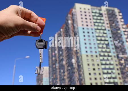 Hausschlüssel in männlicher Hand auf dem Hintergrund neuer Gebäude. Immobilienmakler, Umzug oder Vermietung von Immobilien Stockfoto