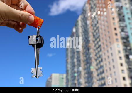 Hausschlüssel in männlicher Hand auf dem Hintergrund neuer Gebäude. Immobilienmakler, Umzug oder Vermietung von Immobilien Stockfoto