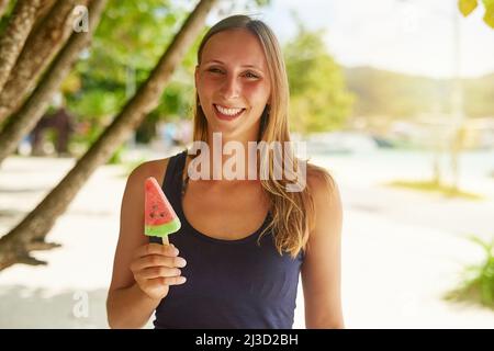 Es ist mein Lieblingssnack im Sommer. Porträt einer attraktiven jungen Frau, die am Strand ein Eis genießt. Stockfoto
