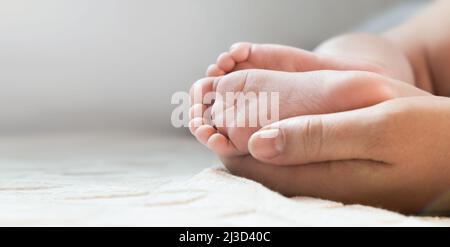 Mutter hält Babyfüße in den Händen. Beine Neugeborene in der Hand weiblicher Eltern. Kleine Kinderfüße. Nahaufnahme. Kleine Zehen des Kindes. Muttertagsurlaub Stockfoto