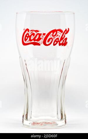 Nahaufnahme der unverwechselbaren und erkennbaren Form eines leeren Coca Cola-Markenglases mit alkoholfreien Getränken, wobei die Unterschrift des Markenzeichens rot hervorgehoben ist. Stockfoto