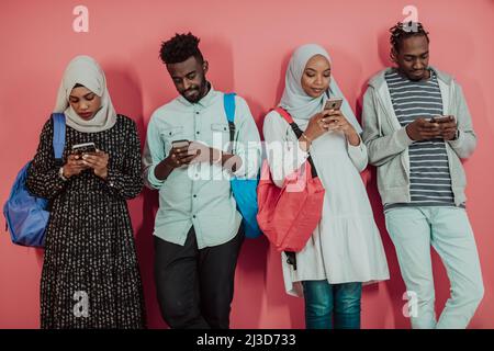 Eine Gruppe afrikanischer muslimischer Studenten benutzt Smartphones, während sie vor einem rosa Hintergrund stehen Stockfoto