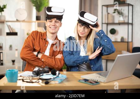 Junges Paar in Freizeitkleidung, das während der Freizeit zu Hause ein VR-Headset und einen Laptop verwendet, um Spiele zu spielen. Konzept von Familie und Unterhaltung. Stockfoto