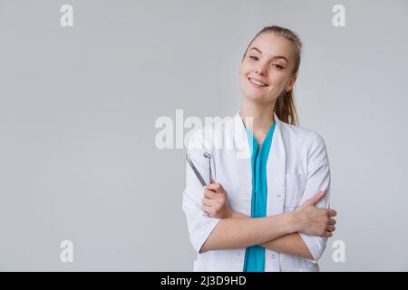 Junge Zahnärztin in Uniform mit Pinzette und Spiegel isoliert auf weiß Stockfoto
