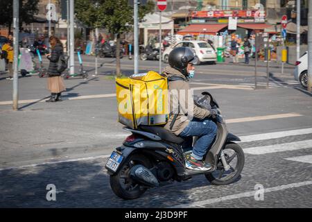 Neapel, Italien - 25. März 2022: Glovo, Junge liefert Lebensmittel zu Hause mit dem Roller im speziellen Thermomucksack. Stockfoto