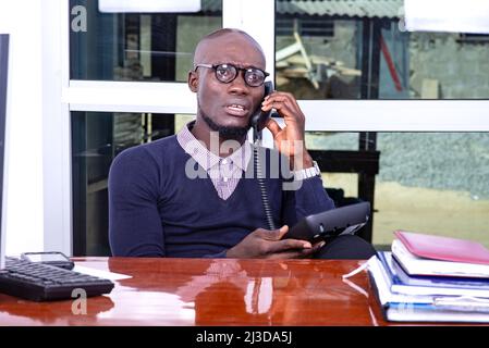 Ein gutaussehender Geschäftsmann in einem Polohemd sitzt am Schreibtisch und redet am Telefon und sieht besorgt aus. Stockfoto
