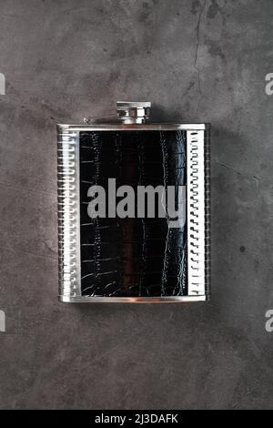 Taschenflasche aus Stahl in Lederoptik mit einem alkoholischen Getränk auf dunklem Hintergrund mit Kopierfläche Stockfoto