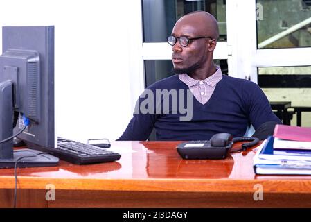 Ein hübscher Geschäftsmann in einem Poloshirt sitzt am Schreibtisch und schaut auf den Laptop-Bildschirm. Stockfoto