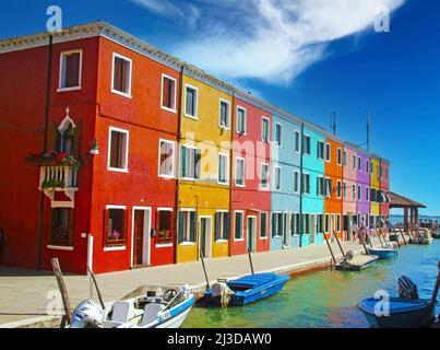 Venedig (burano), Italien - Mai 9. 2019: Blick auf Reihe Helle bunte Häuser am Wasser Kanal mit Booten gegen clearblue Himmel, flauschige Wolken Stockfoto