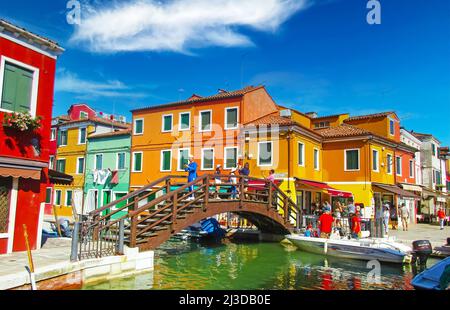 Venedig (Insel Burano), Italien - Mai 9. 2019: Blick auf den Wasserkanal mit Booten, Holzbrücke tre ponti, Touristenmassen, wieder knallbunte Häuser Stockfoto