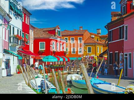 Venedig (Burano), Italien - Mai 9. 2019: Blick über den Wasserkanal mit Booten auf bunt gefärbte Häuser und Tre ponti Brücke, blauer Himmel, flauschige Wolke Stockfoto