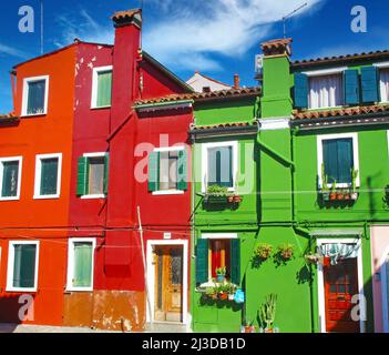 Venedig (Burano), Italien - Mai 9. 2019: Blick auf helle bunte Hausfassaden in grün, rot und ockerfarben, blauer Himmel Stockfoto