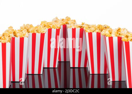 Kino-, Film- und Theaterkonzept. Popcorn-Boxen mit weißen und roten Streifen voller Süße mit Karamell-Popcorn auf schwarzem reflektierendem Hintergrund in Weiß Stockfoto