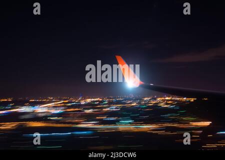 Nachtlandung nähern Sie sich dem Flughafen über die Lichter der Stadt, Blick auf den Flügel des Flugzeugs, Schießen mit einer langen Belichtung Stockfoto