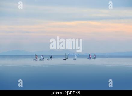 Segelboote und Schiffe bei Sonnenuntergang. Blaues Meer und schöner Himmel mit Segelbooten. Ägäis, Mittelmeer, Griechenland Stockfoto