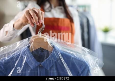 Der Administrator der Reinigungskräfte hält saubere Kleidung auf Kleiderbügeln in der Tasche Stockfoto