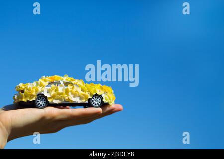 Ein Spielzeugauto mit gelben Blumen in einer Hand über dem blauen Himmel Stockfoto