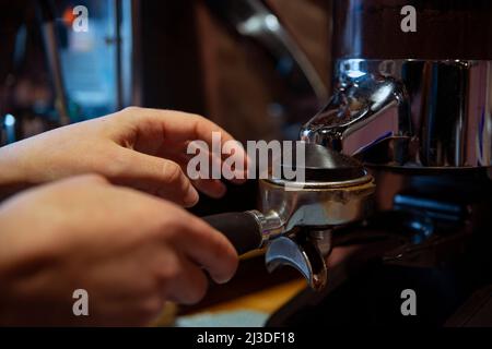 Der Barista manipuliert den gemahlenen Kaffeesatz in einem Portafilter und bereitet Espresso zu Stockfoto