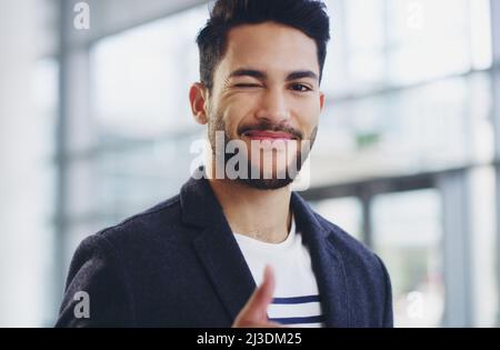 Ich habe das. Eine kurze Aufnahme eines jungen Geschäftsmanns, der beim Gehen durch ein modernes Büro zwinkert und Daumen nach oben zeigt. Stockfoto