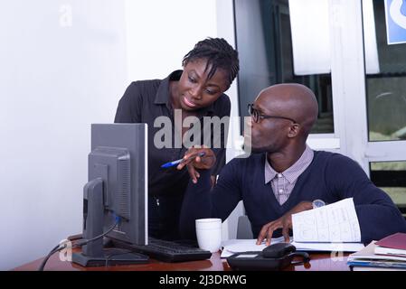 Geschäftsmann und Sekretärin arbeiten zusammen auf einem Laptop im Büro. Geschäftsmann zeigt etwas auf dem Computerbildschirm. Stockfoto