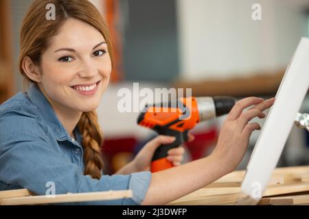 Weibliche Arbeiterin, die orangefarbene Bohrer auf Holzstücken verwendet Stockfoto