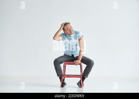 Brutaler Mann in einem Hemd mit kurzen Ärmeln, der auf dem Stuhl sitzt, seine Fäuste geballt, leicht gebeugt, unter dem Blick der Stirn Stockfoto