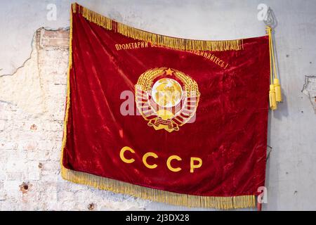 Die alte rote Flagge der Sowjetunion mit dem goldenen Wappen befindet sich auf einer grungigen Wand Stockfoto