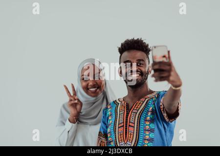 Ein junges afrikanisches Paar, das ein Selfie auf ihrem Smartphone macht, meine Schuhe in traditioneller sudaneser Kleidung. Selektiver Fokus. Stockfoto