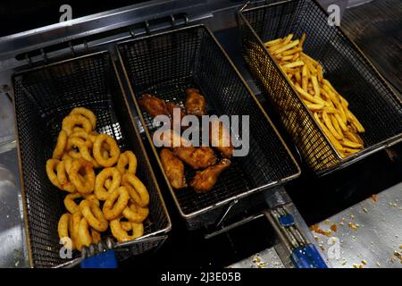 Frittierte Snacks in einem fetten Frittierkorb, pommes Frites, Zwiebelringe und Flügel usw. Stockfoto