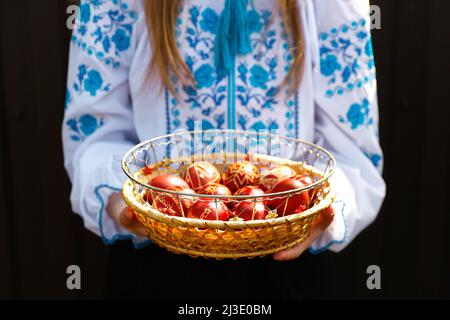 Unschärfe ukrainische Mädchen in vyschywanka hält Korb von farbigen roten Eiern auf schwarzem Hintergrund. Ostern, Ukraine. Basteln Sie Eier. Sammlung von Pysanka oder kra Stockfoto